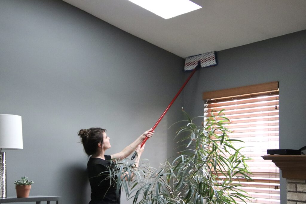 woman dusting and cleaning gray wall